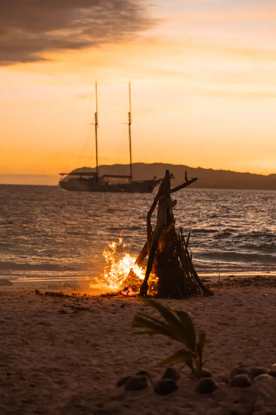 Beach bonfire at sunset beside a phinisi