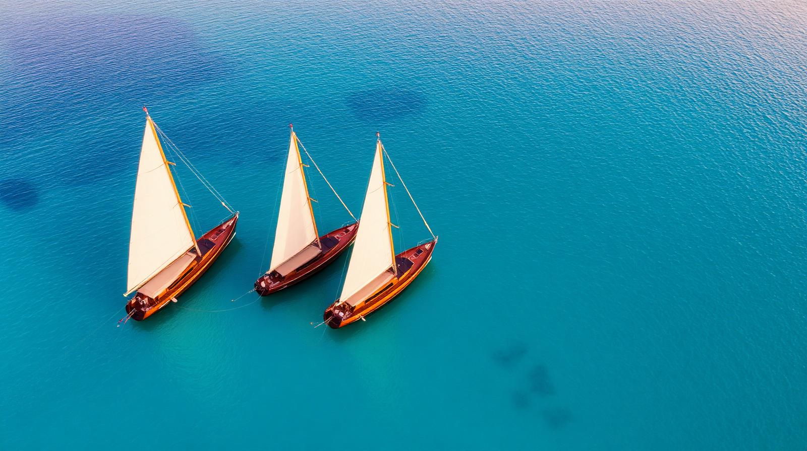 Three luxury Indonesian phinisi sailing yachts anchored together in turquoise water at golden hour