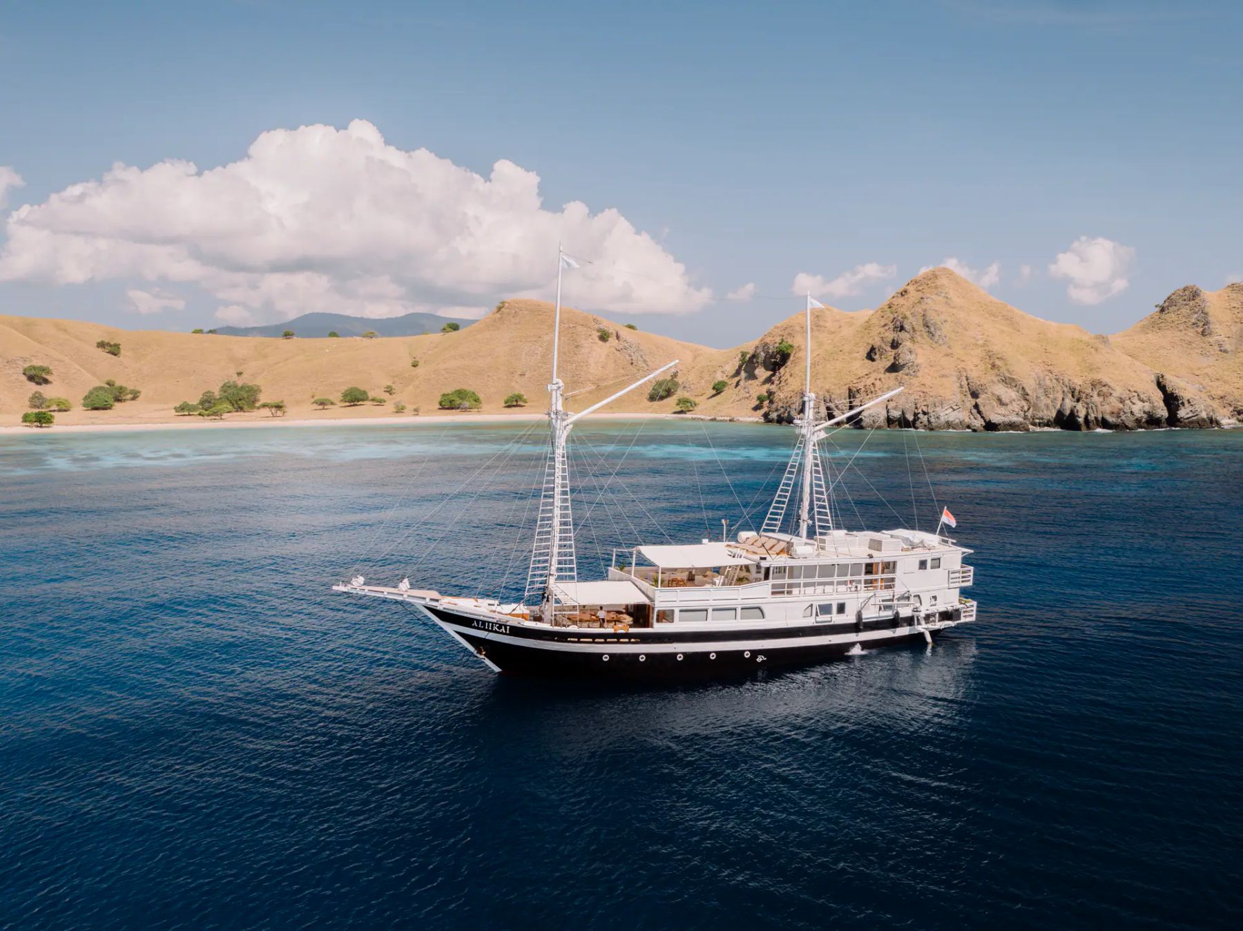 Vista aérea del yate de chárter privado Aliikai anclado en aguas turquesas frente a una isla de Komodo