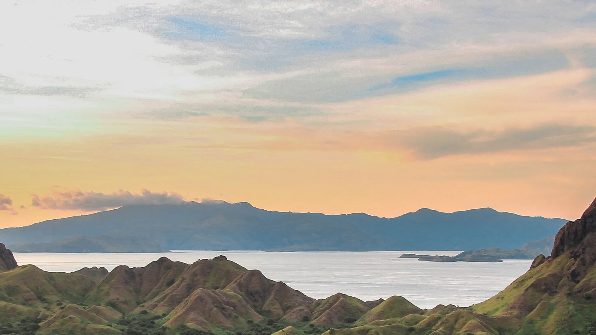 Hills and sheltered bays of Komodo National Park glowing at sunset above calm sea