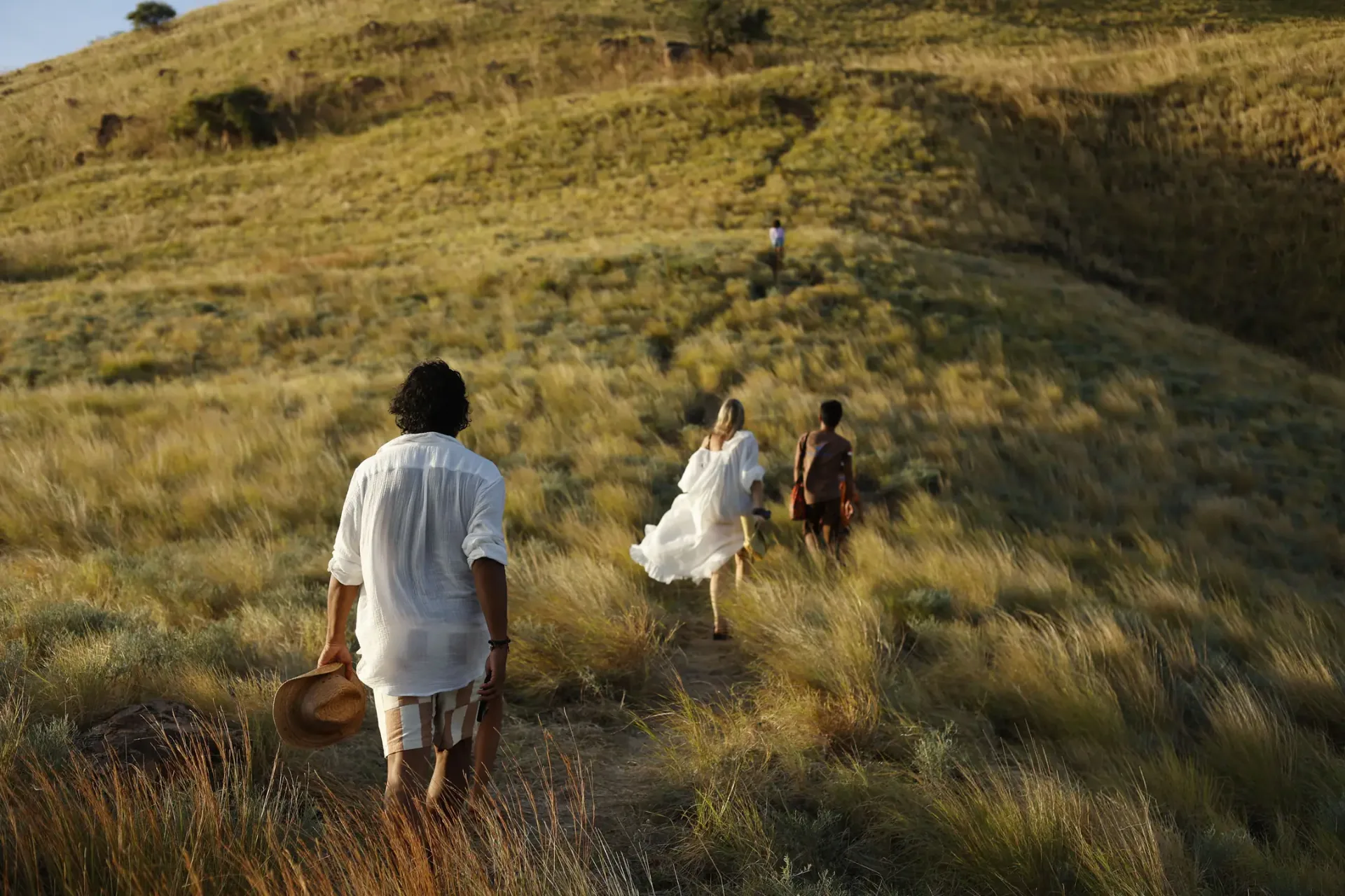 Guests hiking golden grassland hills sunset trek Komodo Island adventure