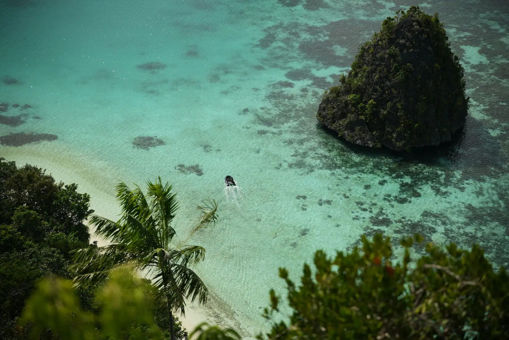 Speedboat in crystal lagoon near karst rock Raja Ampat